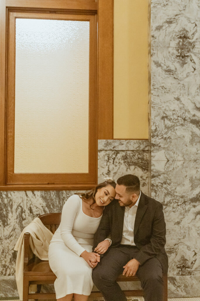 Couple sitting on a bench inside the courthouse waiting to elope.