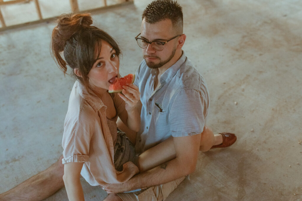 Couple sitting on the floor eating watermelon.