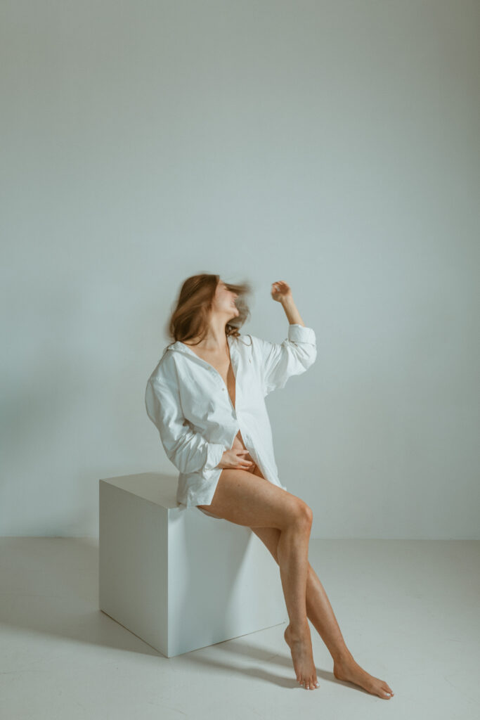 Woman sitting on a white wooden board block during her maternity photoshoot.