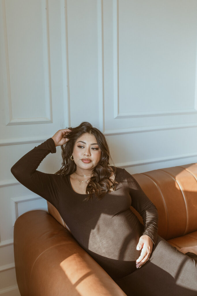 Women sitting on the couch with her hand on her belly for her maternity photoshoot.