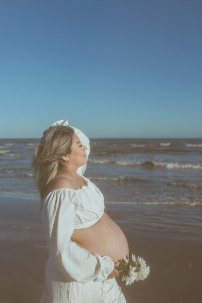 Woman by the beach holing her pregnant belly. 