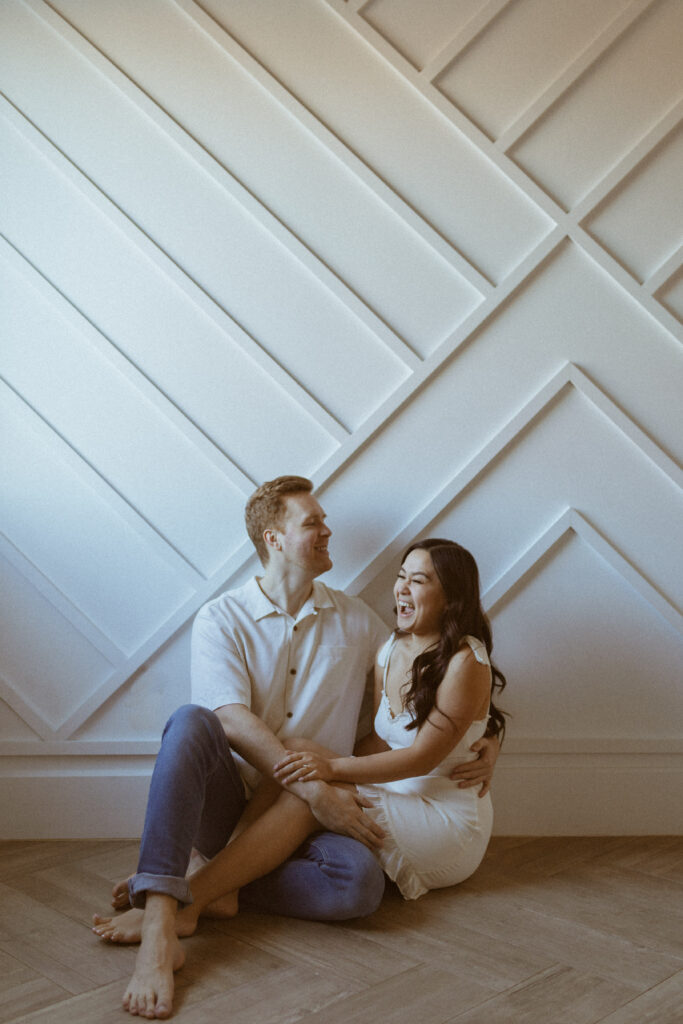 Couple sitting on the floor, laughing during their engagement photos. 