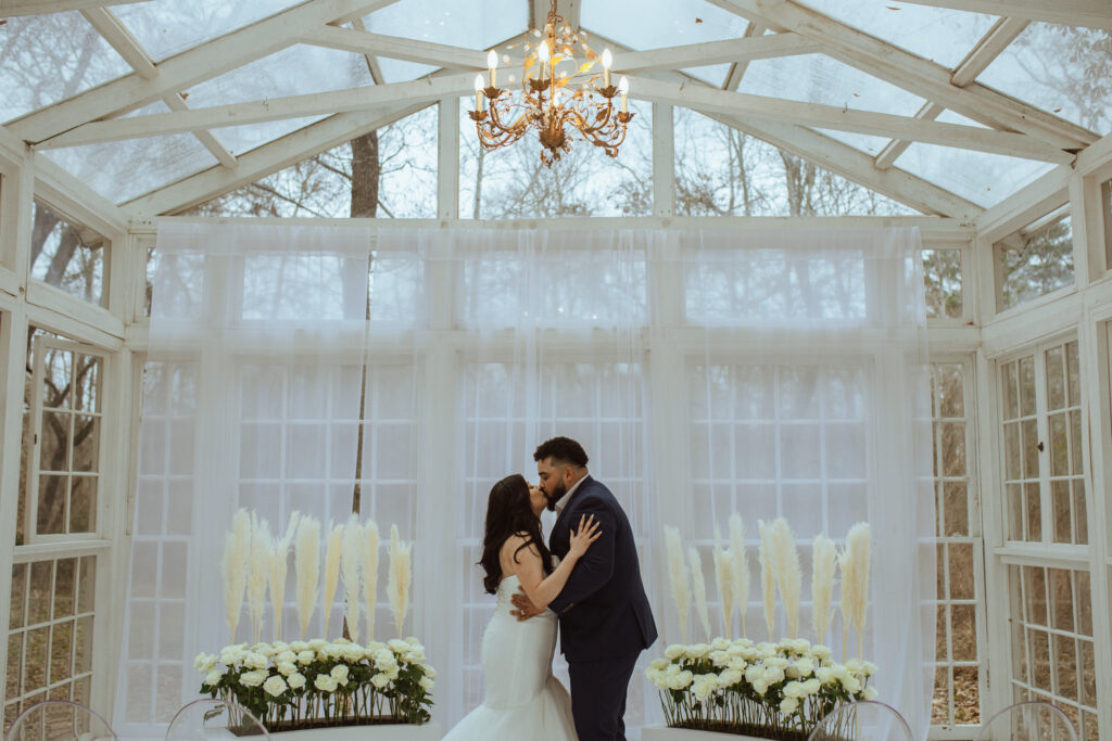 Bride and groom kissing during their wedding inside a green house