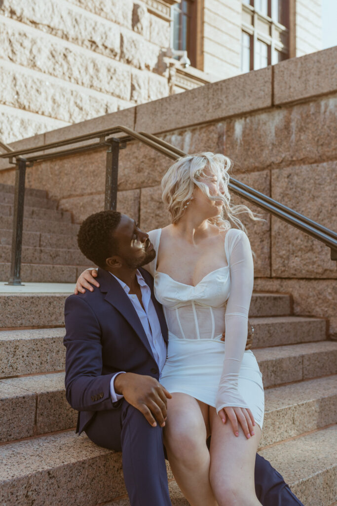 Couple sitting on the steps on a courthouse during a winter photoshoot.