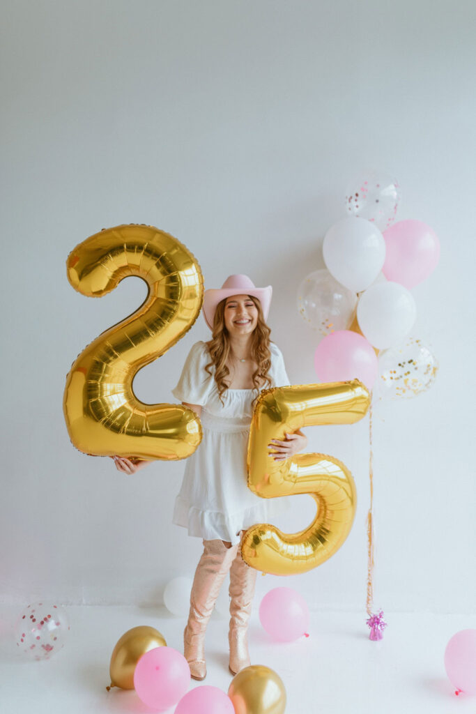 Girl sitting with a cowgirl hat and number 25 balloons for her cowgirl birthday photoshoot 