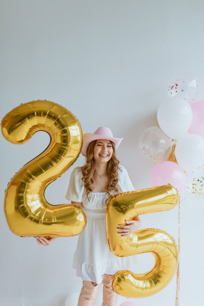 Girl sitting with a cowgirl hat and number 25 balloons for her cowgirl birthday photoshoot 