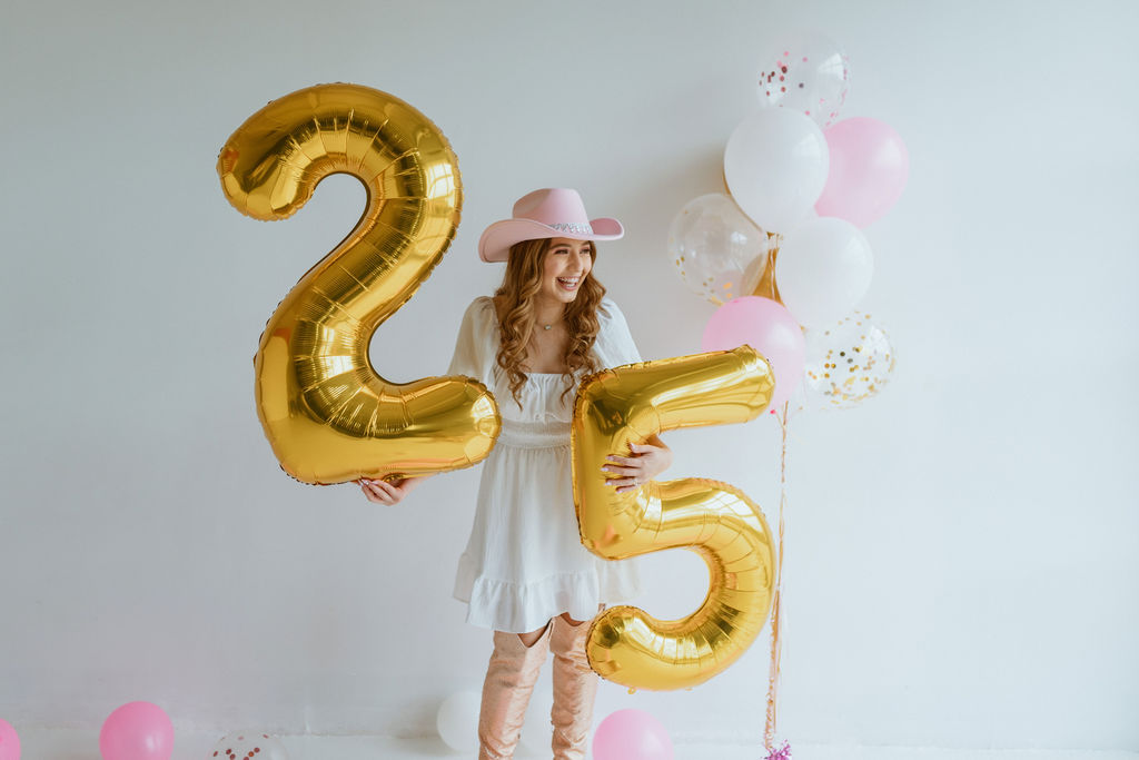 Girl sitting with a cowgirl hat and number 25 balloons for her cowgirl birthday photoshoot 