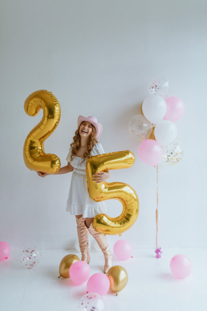 Girl sitting with a cowgirl hat and number 25 balloons for her cowgirl birthday photoshoot 