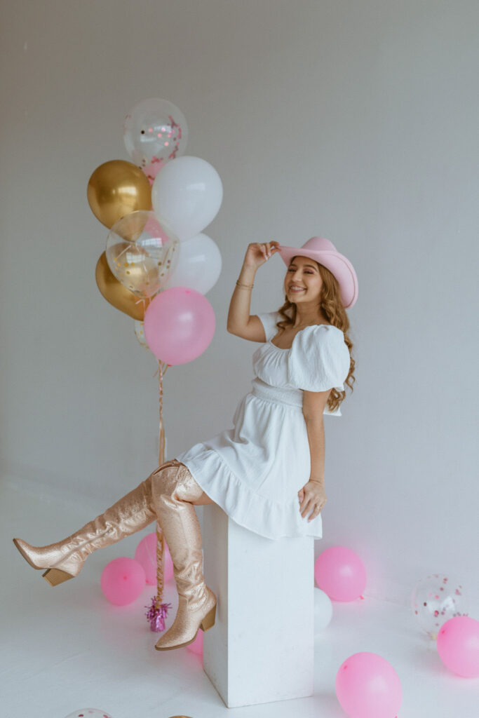 Girl sitting with a cowgirl hat and balloons for her cowgirl birthday photoshoot