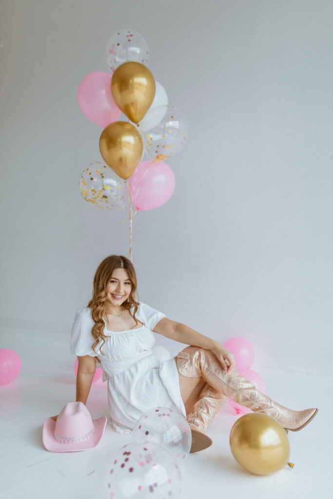 Girl sitting with a cowgirl hat and balloons for her cowgirl birthday photoshoot