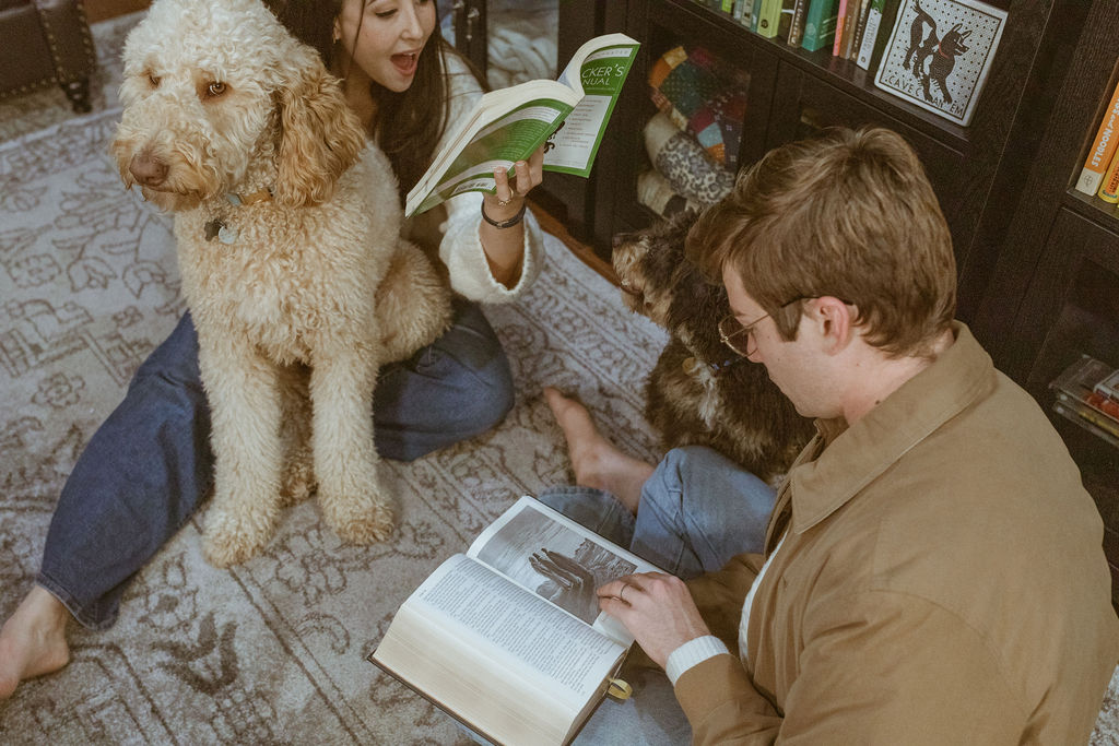 During a fall inspired photoshoot, a  couple is reading books and dogs are next to them. 